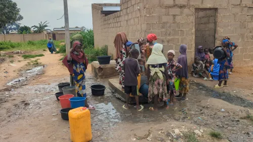 Women and children gather around a street tap in Kano, filling blue, yellow and orange containers with water.
