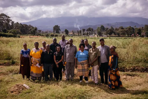 A group of farmers pose together for a photograph in a field near a hill.