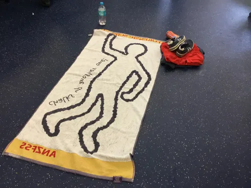 A forensic science mat on the floor. To its top left is a bottle of water, and to its top right are a pair of sneakers and folded clothes.