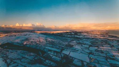 A view of snow-covered hills. Sunlight is seen at the horizon.