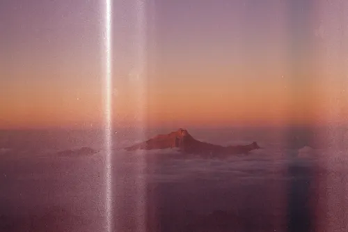 A distant mountain peak rises above a dense sea of clouds during a sunset