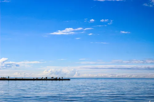 A clear blue sea under a cloudless sky, where a few people stand near the jetty. 
