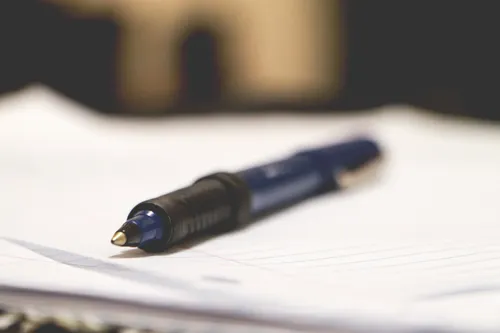 A focused shot of a ball pen placed on lined paper. The background is blurred.