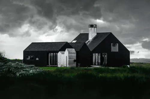 A black-and-white pic of a house with a tall white chimney sits beneath a cloudy sky