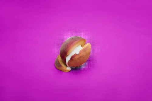 A sliced peach dripping with a thick white cream is placed against a purple background. 