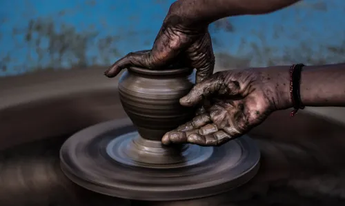 Two hands work on a pottery piece with a black thread tied around the left hand. 