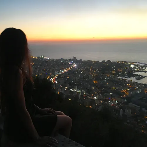 a woman sitting at the edge of a wall overlooking a city