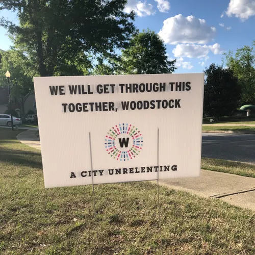 A lawn sign with the words "We will get through this together, Woodstock. A city unrelenting." 