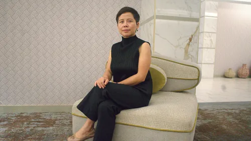 A chinese woman sits in a white room.