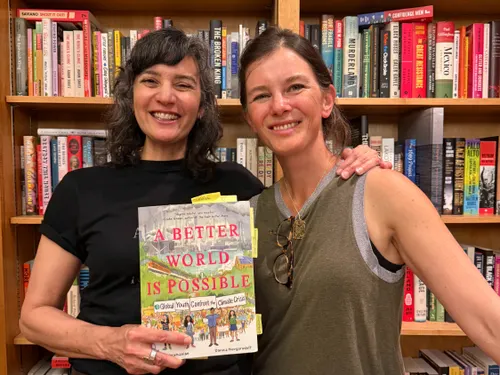 Two women pose with the graphic nonfiction book, "A Better World is Possible"