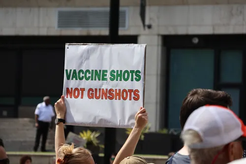 A protester holds up a “VACCINE SHOTS NOT GUNSHOTS” sign 