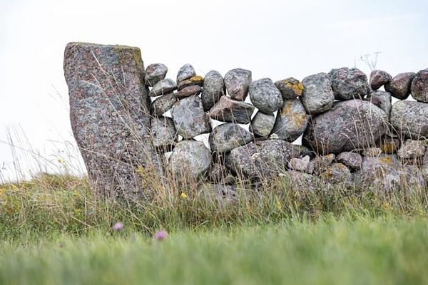 A dry stacked grey stone wall in with grass in the foreground.