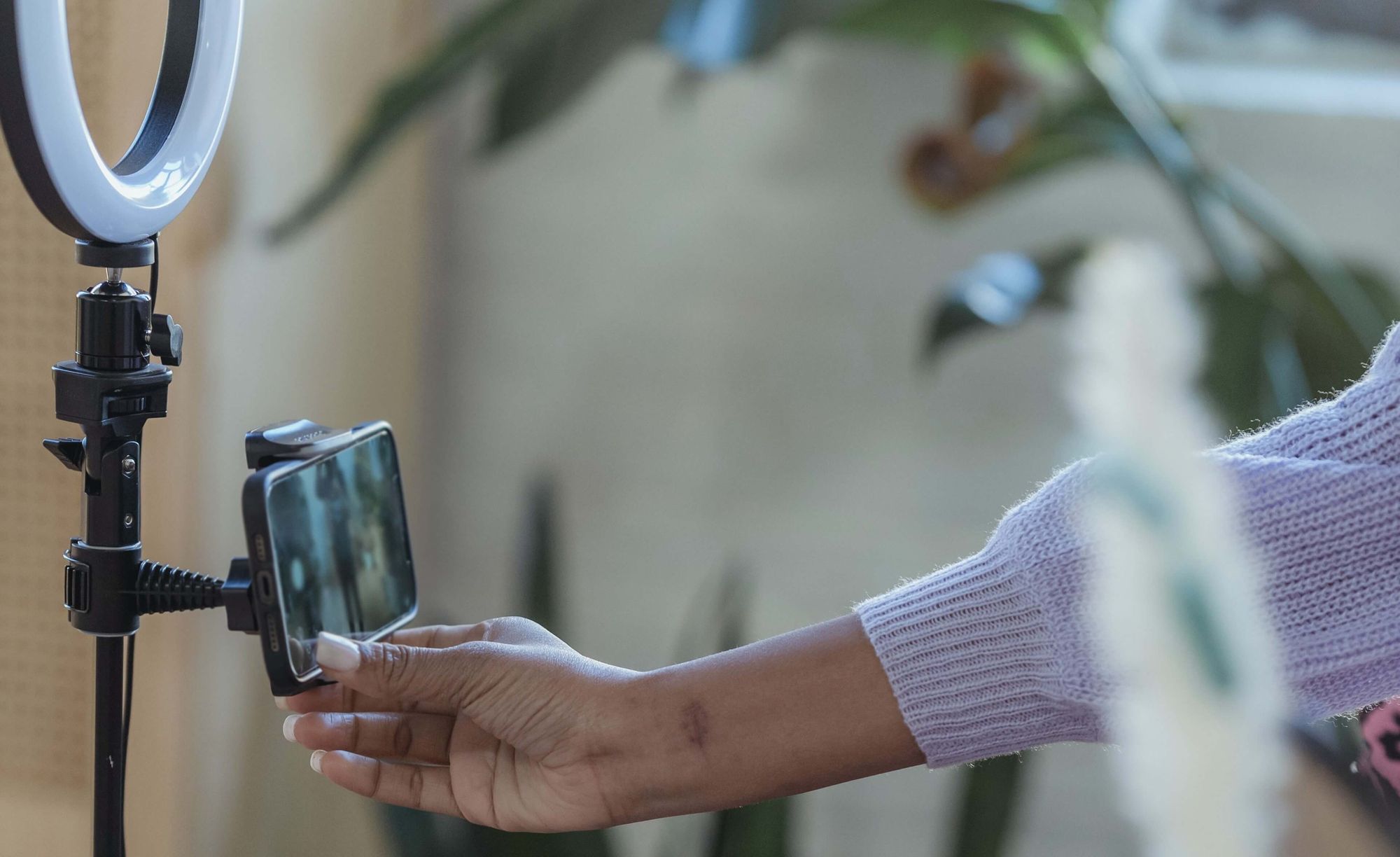 foto de equipamento de ring light com celular acoplado. há uma mão negra de unhas grandes tocando a tela,