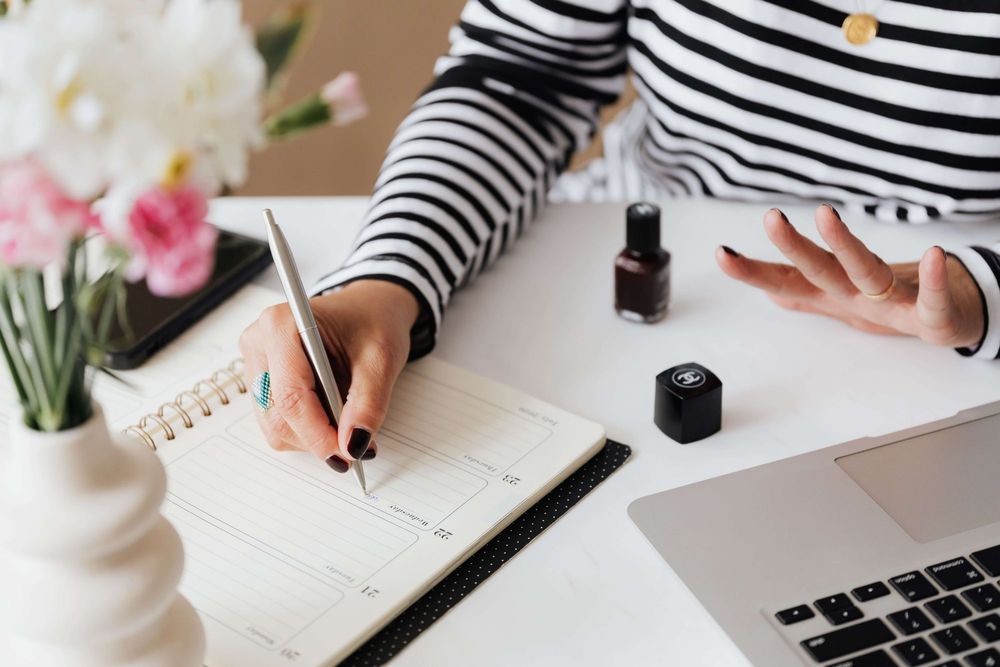 Foto em detalhe de uma mulher fazendo anotações em uma agenda do tipo planner