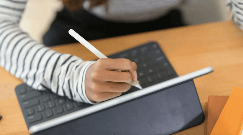Mão feminina sentada em frente a um iPad iniciando um trabalho de ilustração no dispositivo