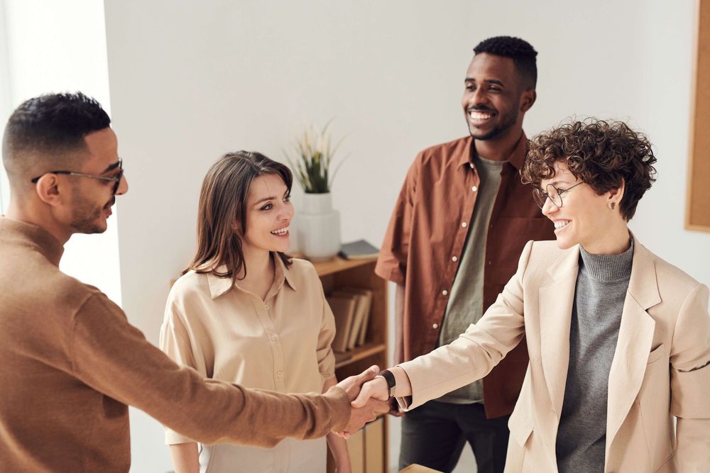 grupo de quatro pessoas, dois homens e duas mulheres, dois deles, uma homem e uma mulher, se cumprimentam em gesto de acordo