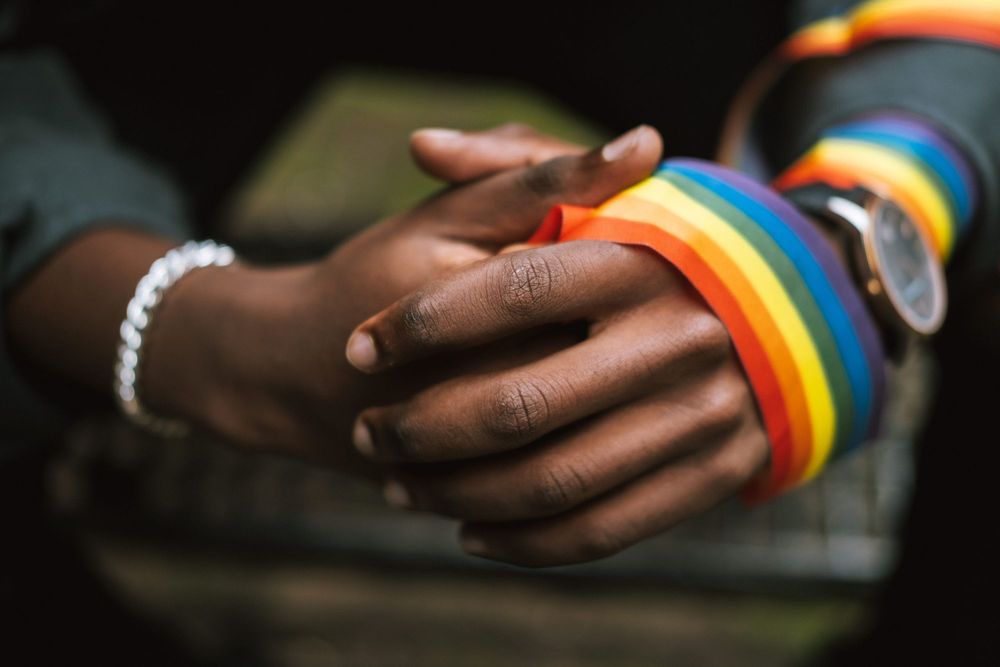mão negras sobrepostas com um pano enrolado no punho, ele tem as cores da bandeira lgbtqia+