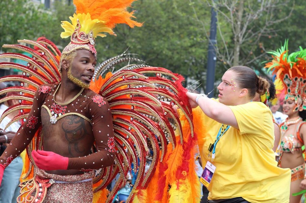 Homem negro em roupa carnavalesca olhando para mulher branca de blusa amarela e crachá 
