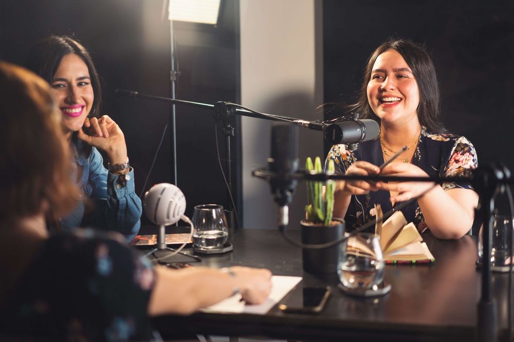 Três mulheres em torno de uma mesa com microfones específicos para podcast