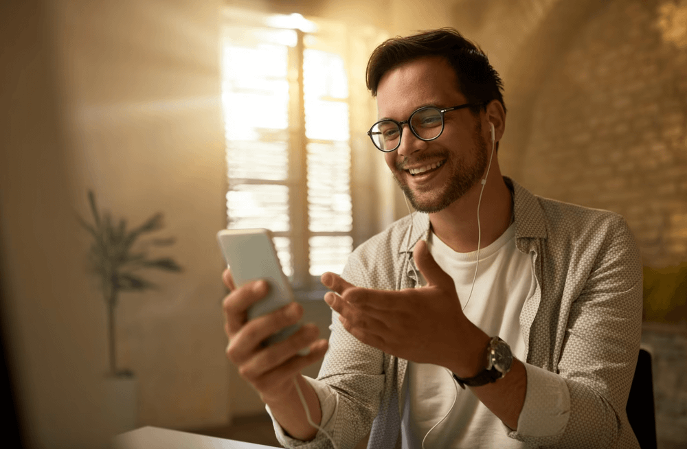 Foto em plano médio de homem branco com barba cerrada segurando um celular e usando fones de ouvido.