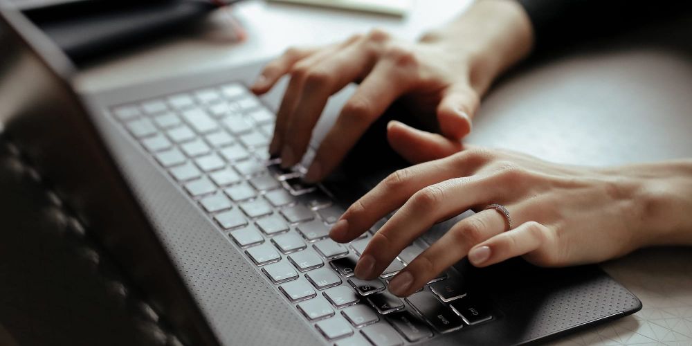 Mão feminina fazendo gestos de digitação em um notebook