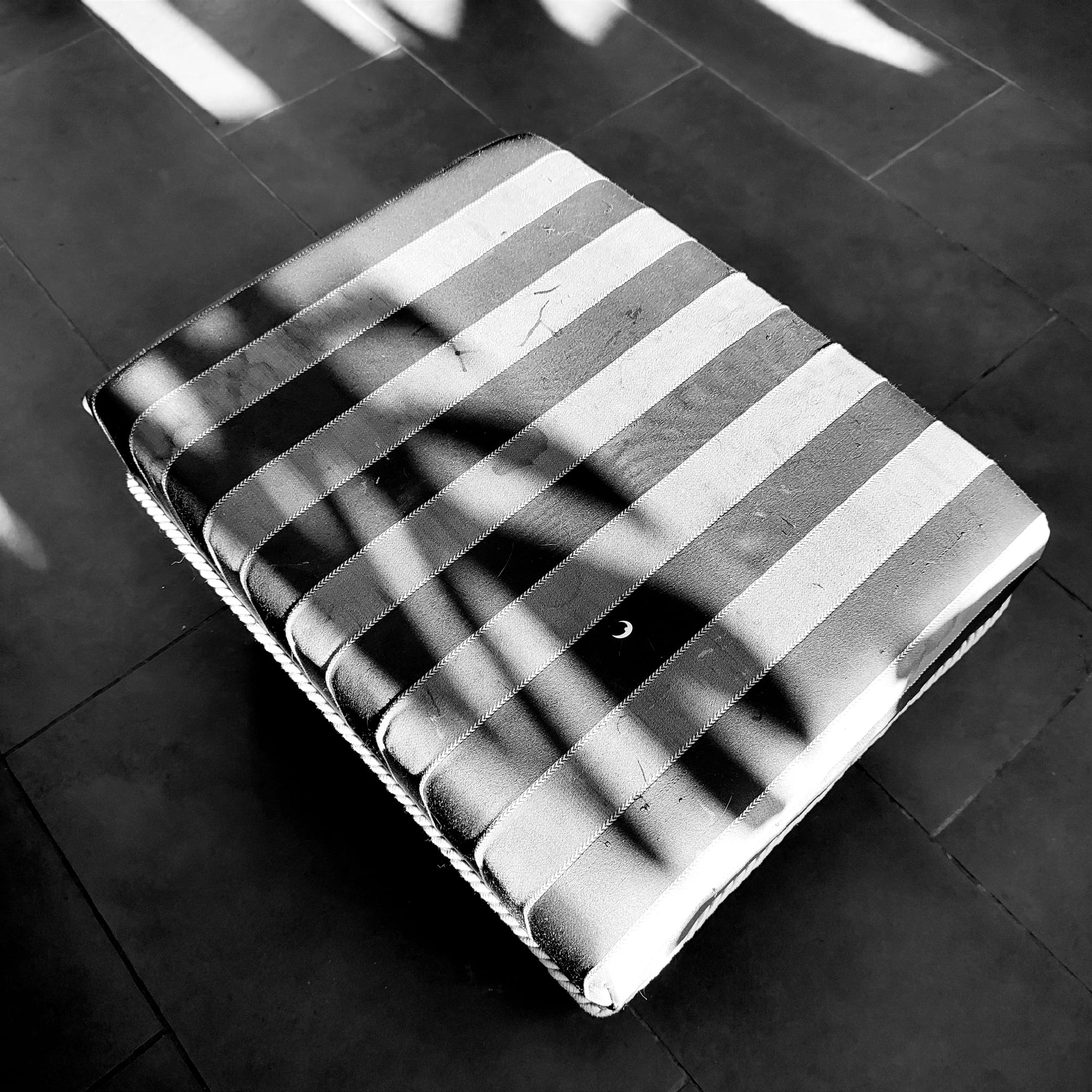 Leaf shadow falling on a footstool and creating a creature with an eye sticker.