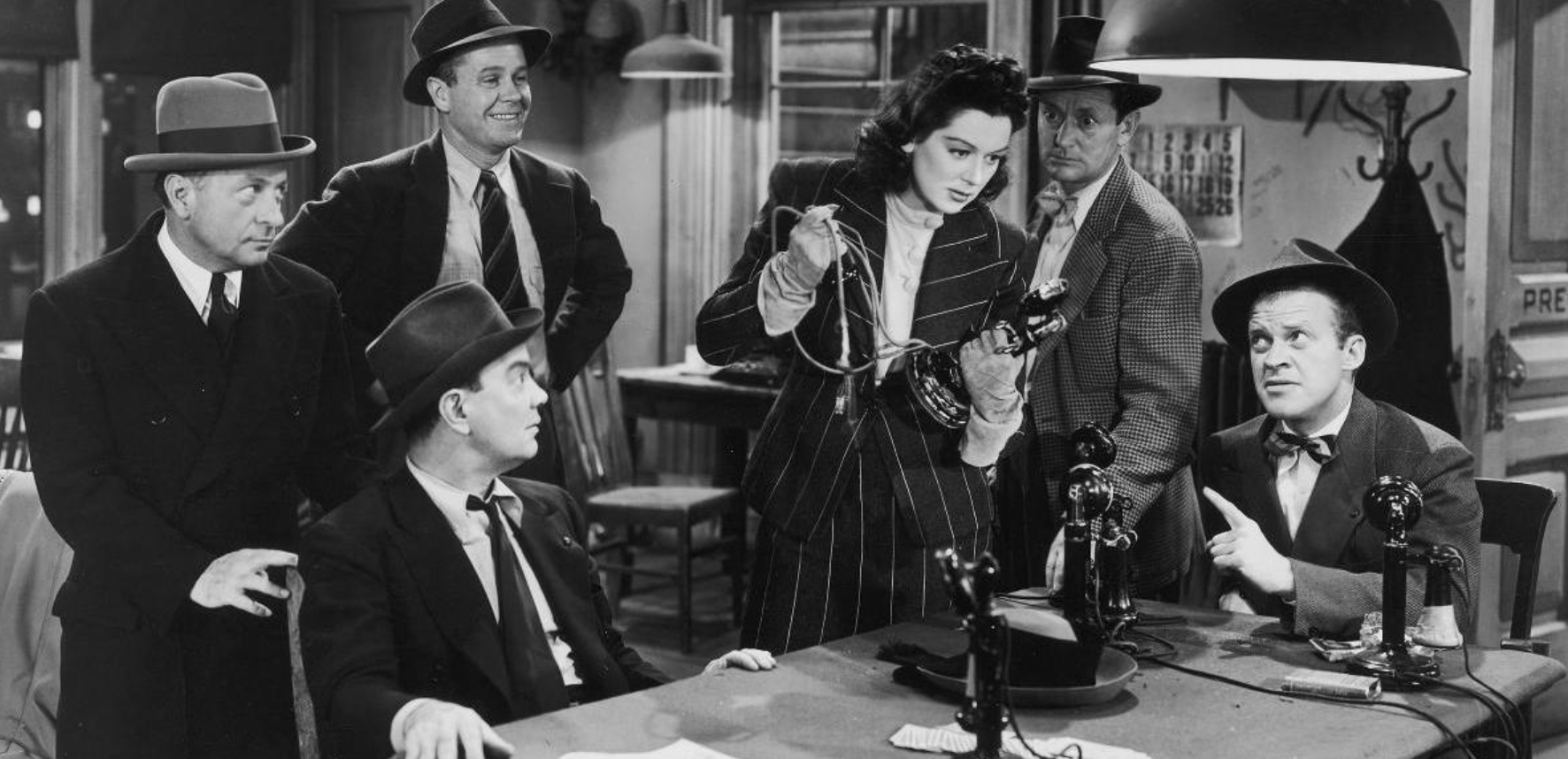 A woman in a wide pinstripe suit clutches and old fashioned phone in an old time pressroom.