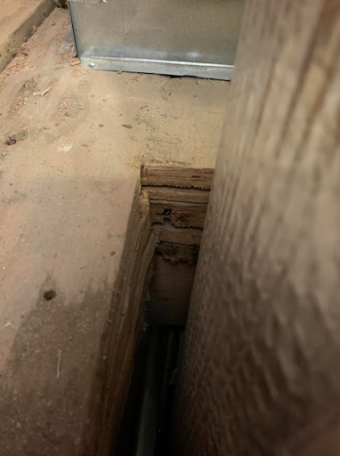 A photo of subfloors next to a wood structural beam going into the basement. There are at least seven layers of material visible piled atop a ceiling joist. It looks like a solid foot of material.