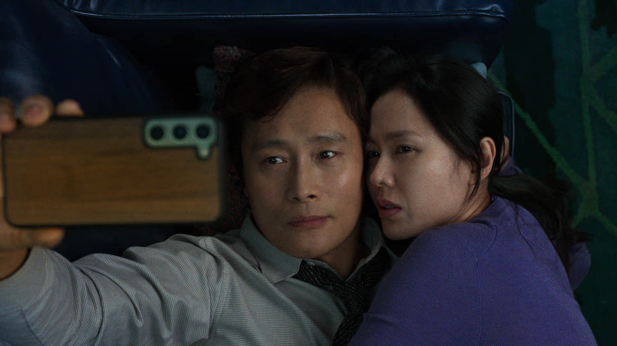 Screenshot from "No Other Choice": Man-su (Lee Byung-hun) and his wife Mi-ri (Son Ye-jin) take a selfie while cuddling on the couch. They seem distressed.