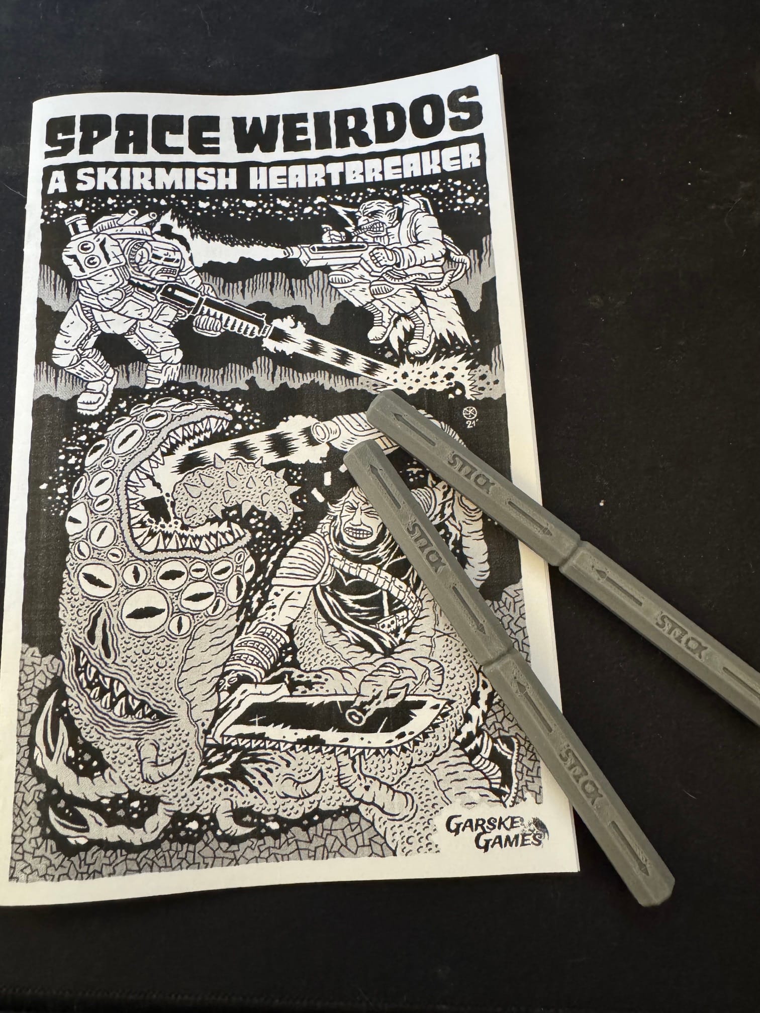 A black-and-white zine-esque manual for Space Weirdos, featuring a heavy metal-style cover featuring various forms of space weirds battling a many-eyed monster.