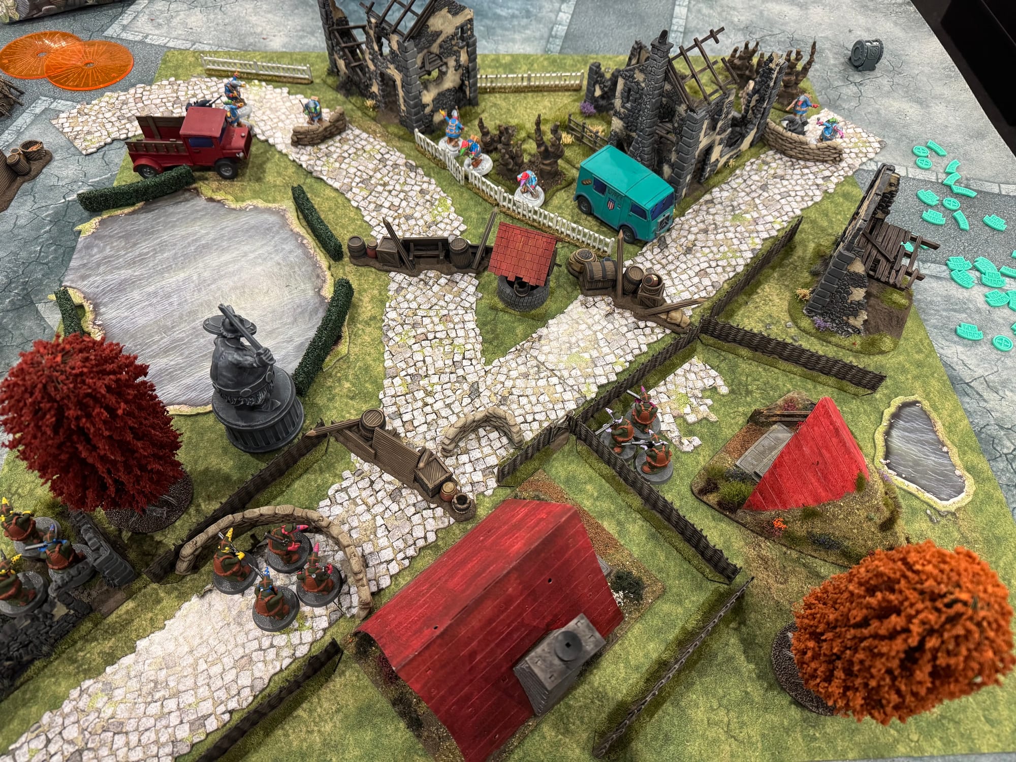 A top down view of a lavishly painted Quar's War battlefield, complete with autumnal trees, crumbling houses, and infantry taking cover.