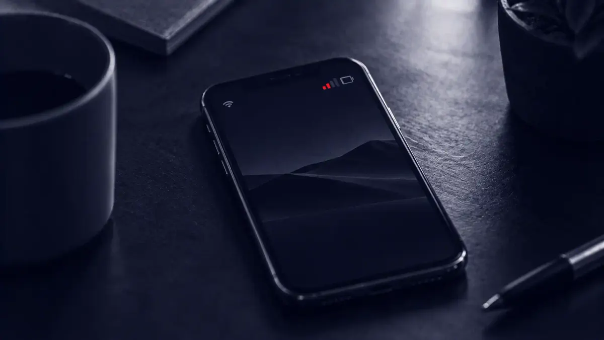Duotone overhead photo of a smartphone lying idle on a desk with no hand near it, its signal bar glowing in signal red.