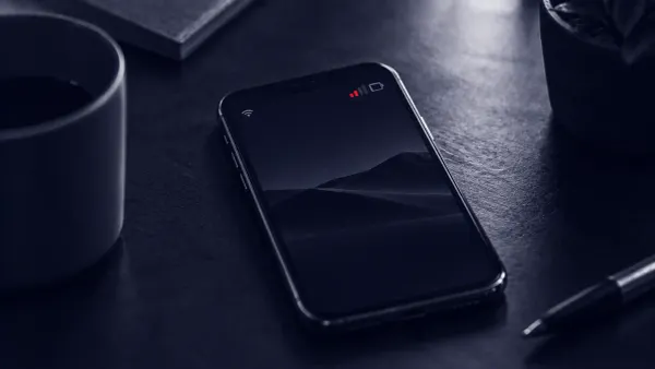 Duotone overhead photo of a smartphone lying idle on a desk with no hand near it, its signal bar glowing in signal red.