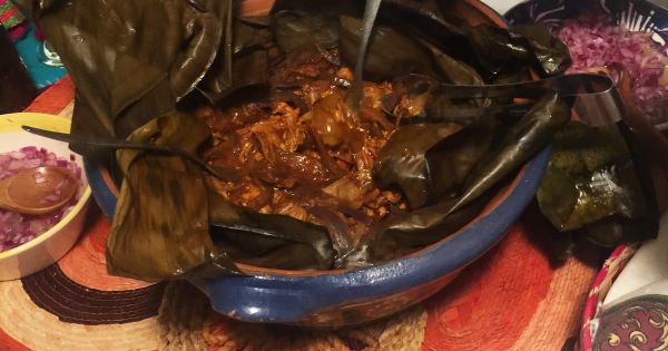 Cochinita pibil-style pork served inside banana leaves with pickled red onions nearby.