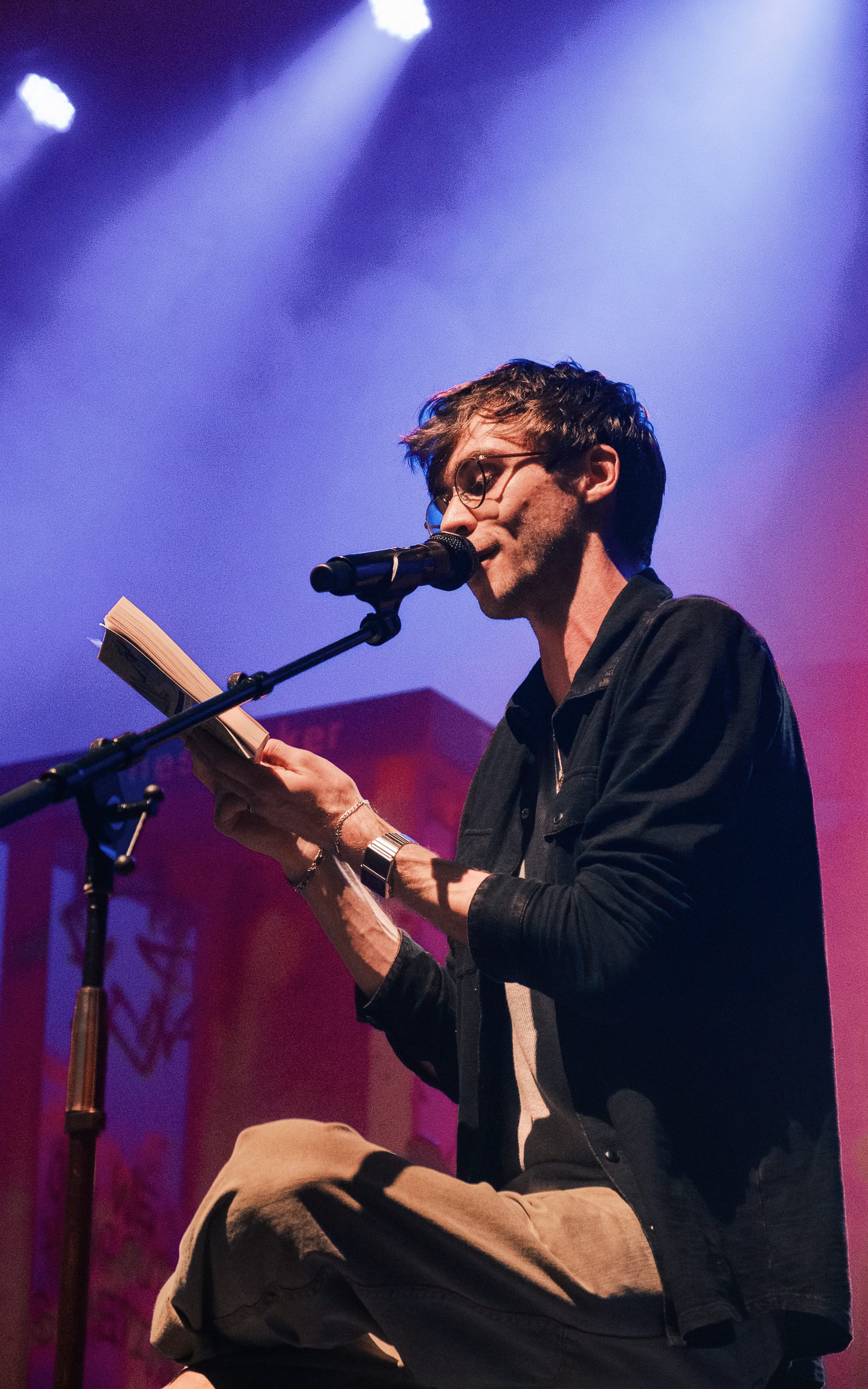 Frosst reading Lord of the Rings to audience members from a book as he sits on a stool.