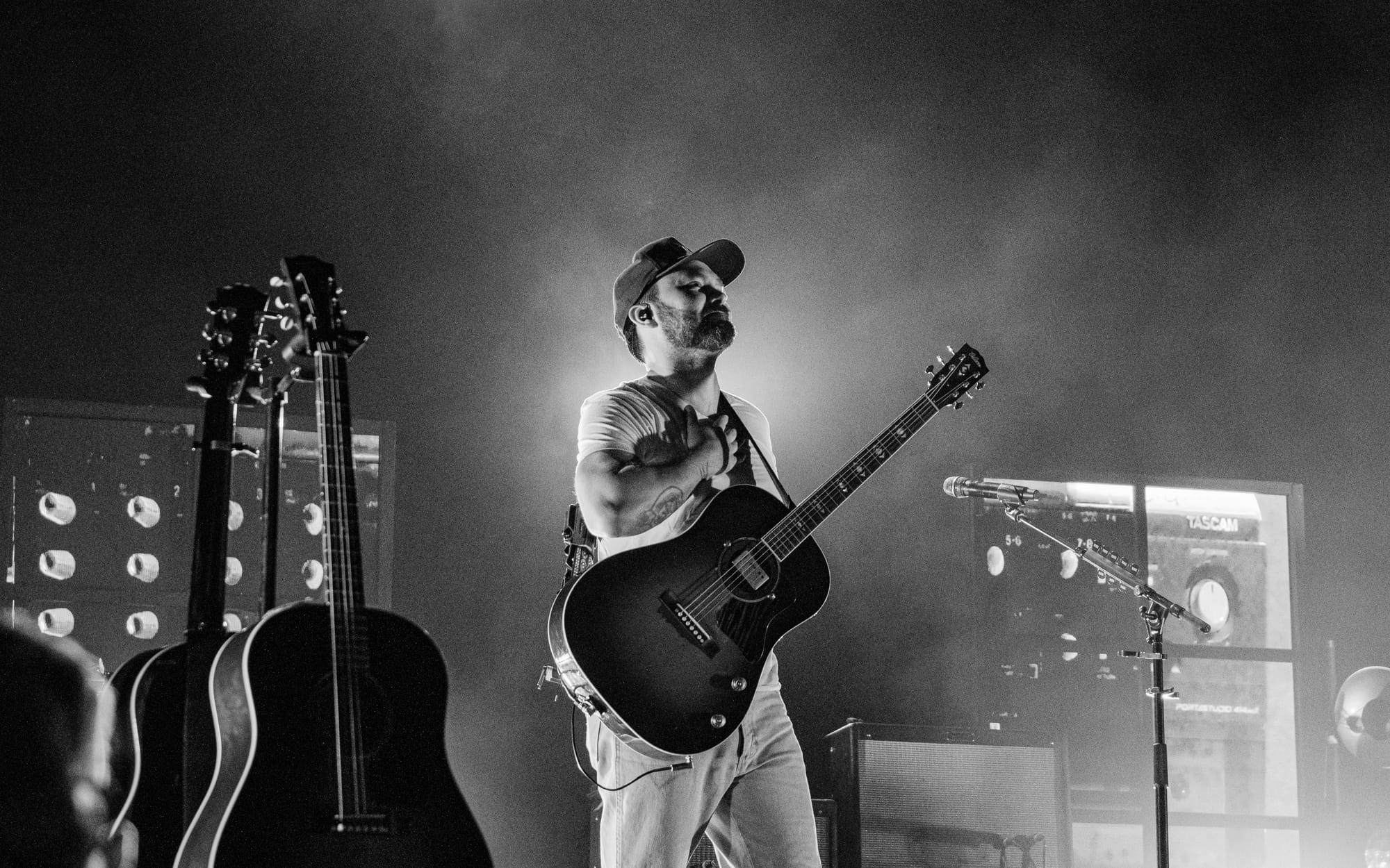 Shakey Graves with a hand to his heart, acoustic guitar slung around his body.