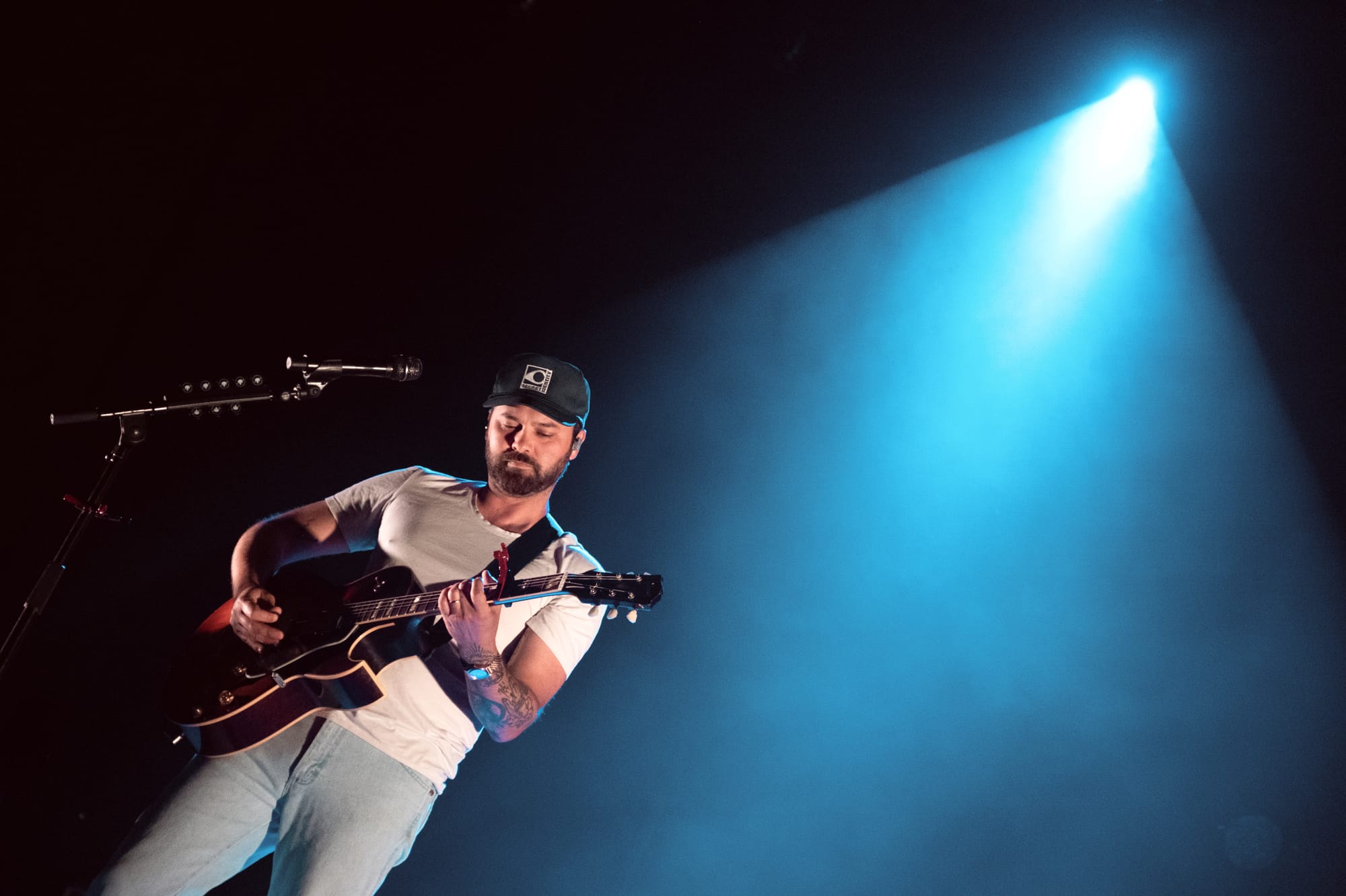 Shakey Graves backlit by light blue spotlighting, playing an acoustic guitar.