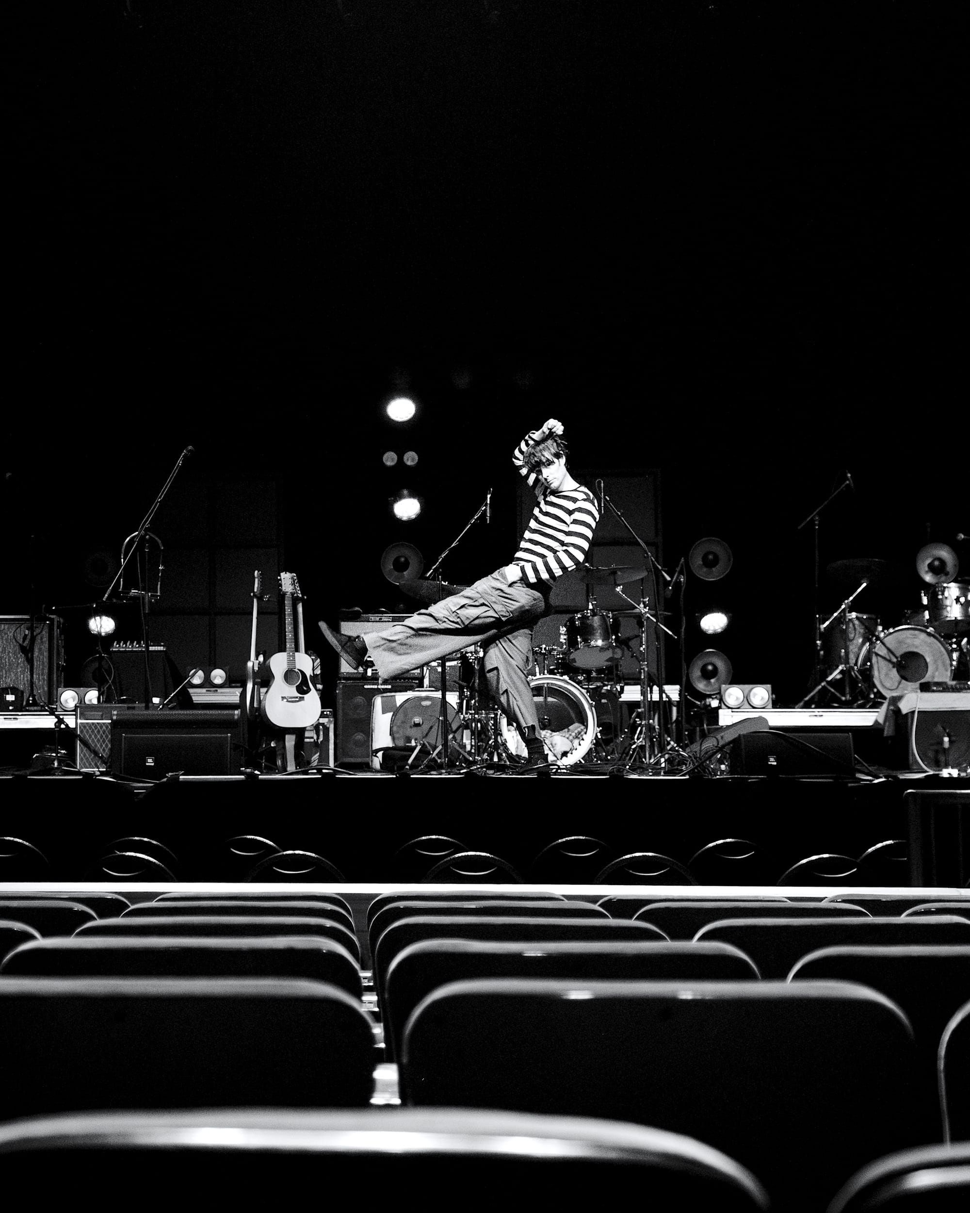 A black-and-white photo of Wes Parker playfully posing on stage in front of rows of empty chairs. 