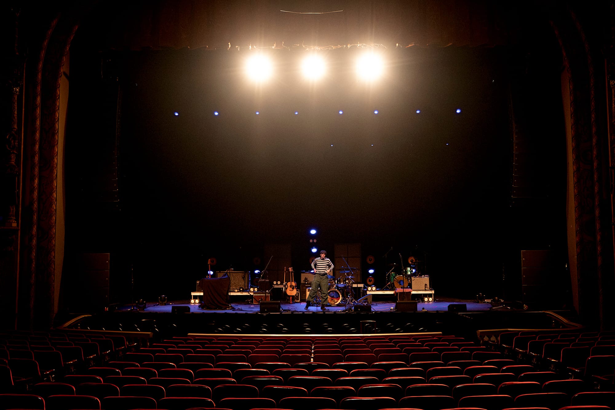 Wes Parker standing centered on stage in a theater in front of rows of empty red seats.