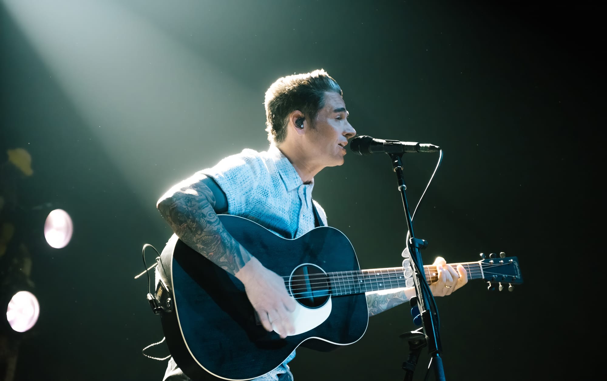 Chris Carrabba of Dashboard Confessional singing into a mic earnestly while backlit by a hazy warm/green-tinted white light.