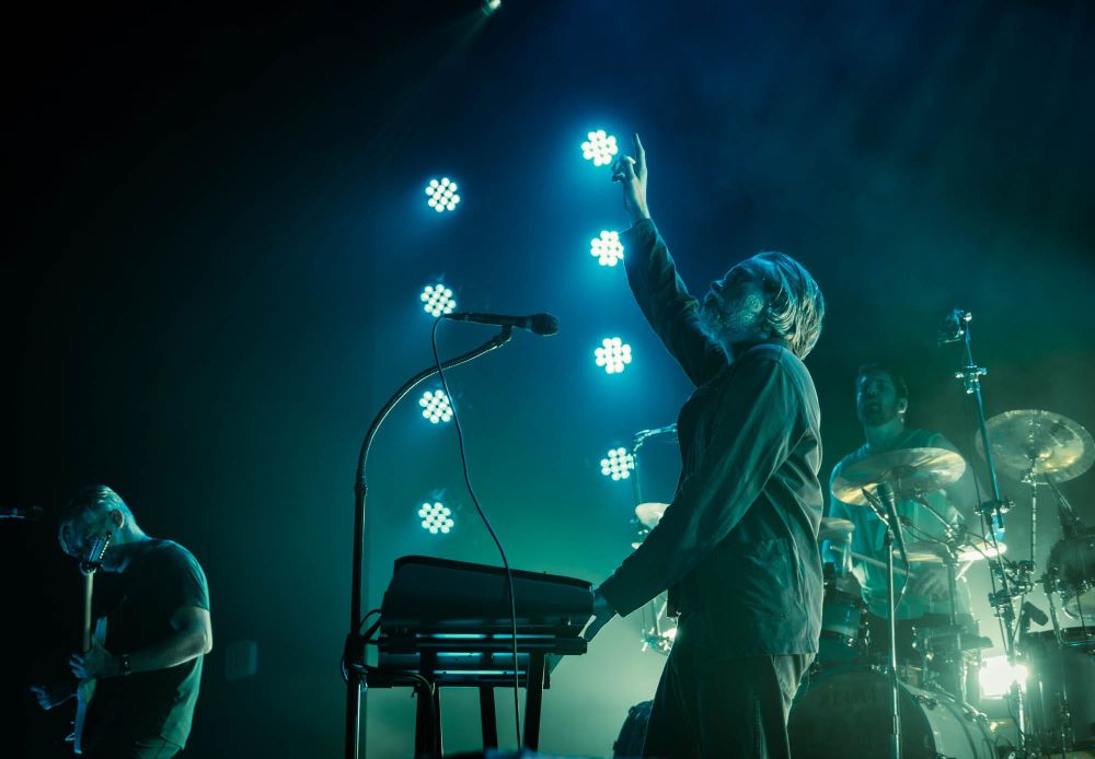 Concert photo of Between the Buried and Me, with vocalist Tommy Giles Rogers standing at the microphone and raising his right arm up