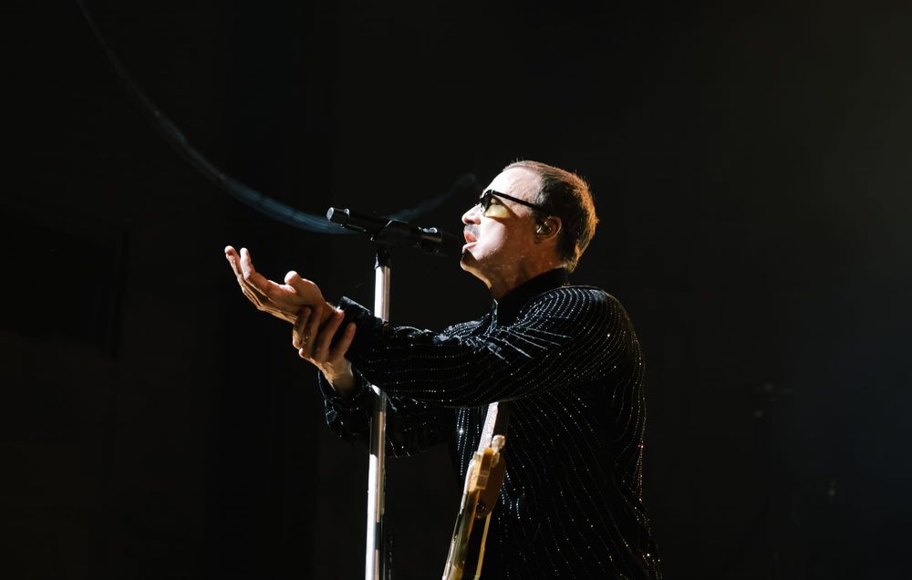 Joe King of The Fray singing passionately into the microphone with outstretched hands. 