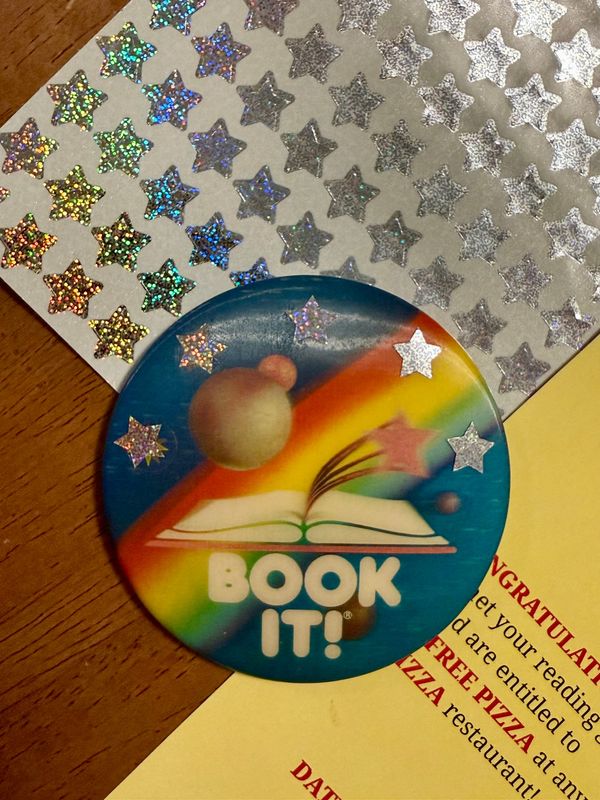 BOOKIT! pin from the 90s, a pack of glitter star stickers, and the bookmark Matt made from last year.