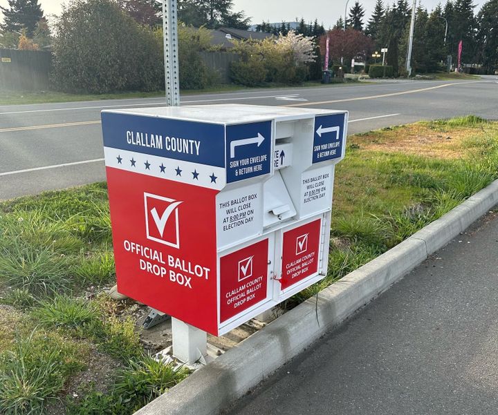 A ballot drop box painted red, white,a nd blue located on a park strip by a county road.