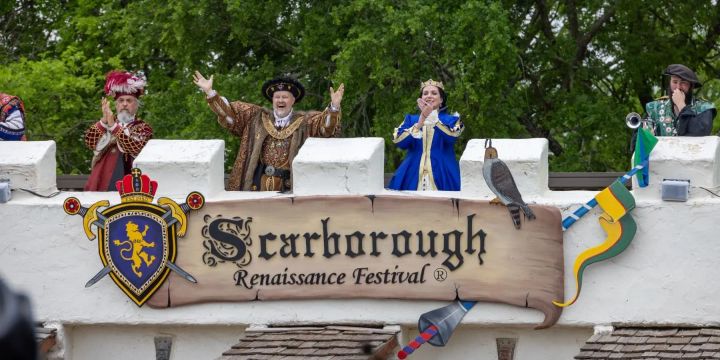 A photo of Scarborough Renaissance Festival royalty cheering above the front gate.