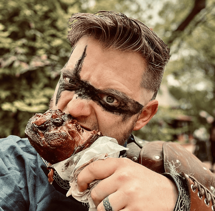 Photo of a man in barbarian attire eating a turkey leg.