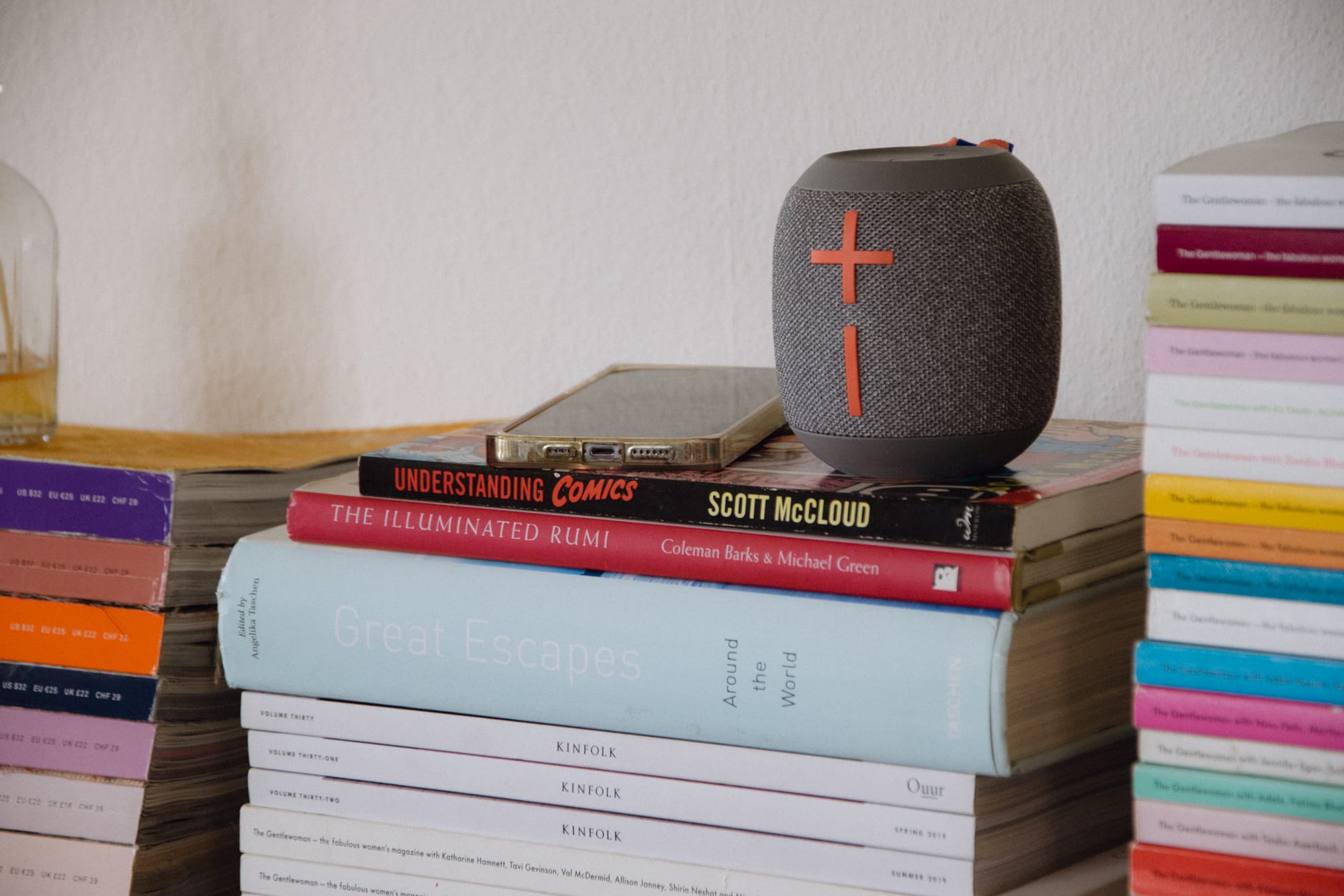 Piles of of magazines and a couple of coffee table books with a wonderboom player and phone sat on top