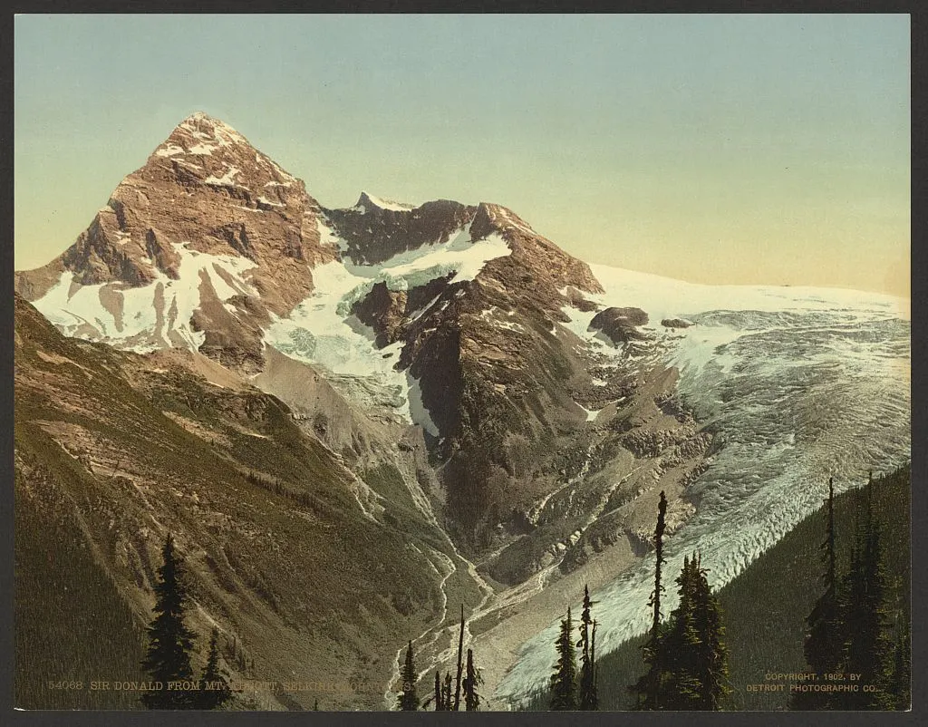 Hand-colored photograph of a glaciered mountain peak above a valley