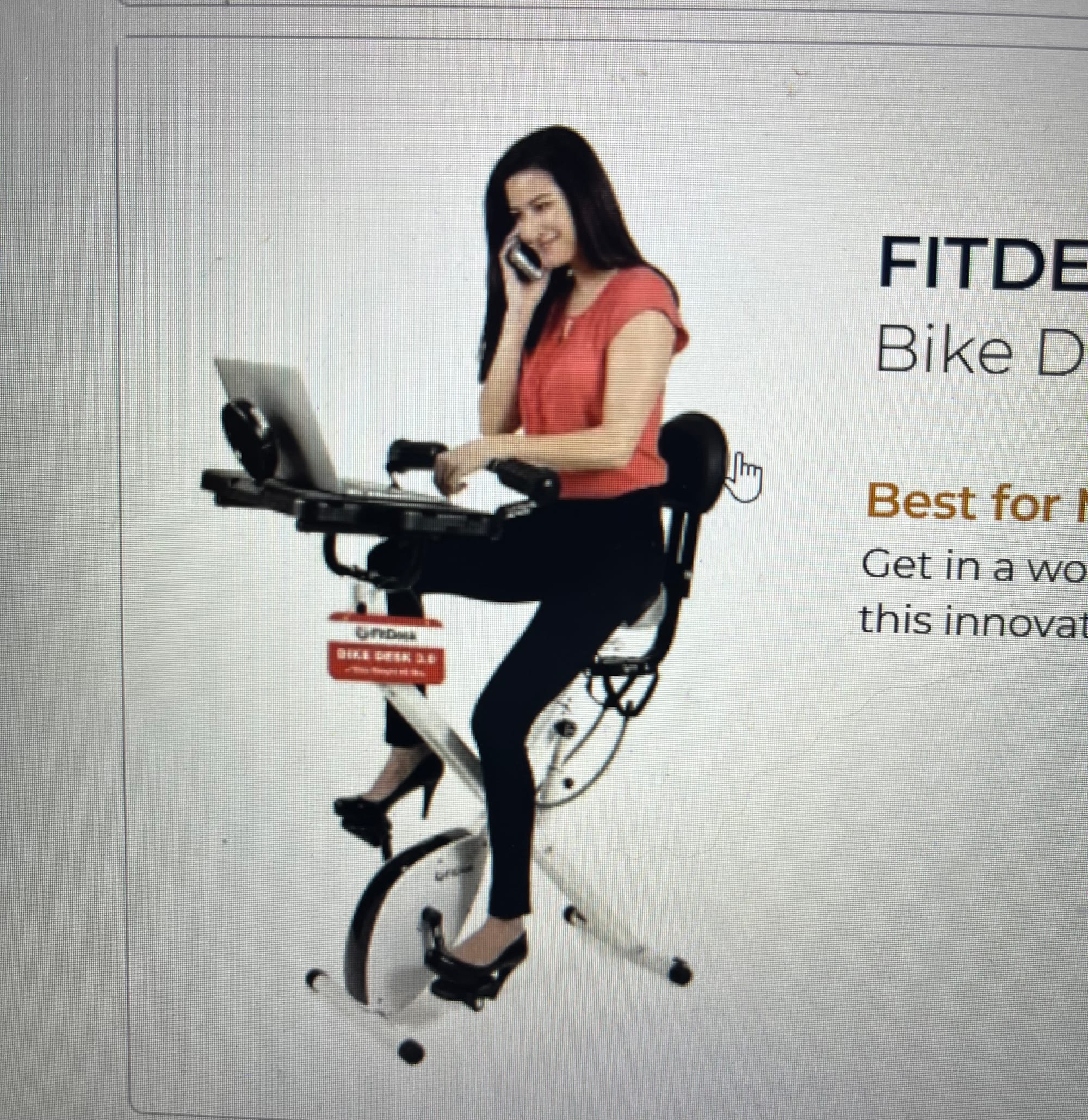 Dark haired woman wearing black heels, black pants, a red short-sleeved blouse sitting on a compact stationary bike with a desk attachment and laptop.