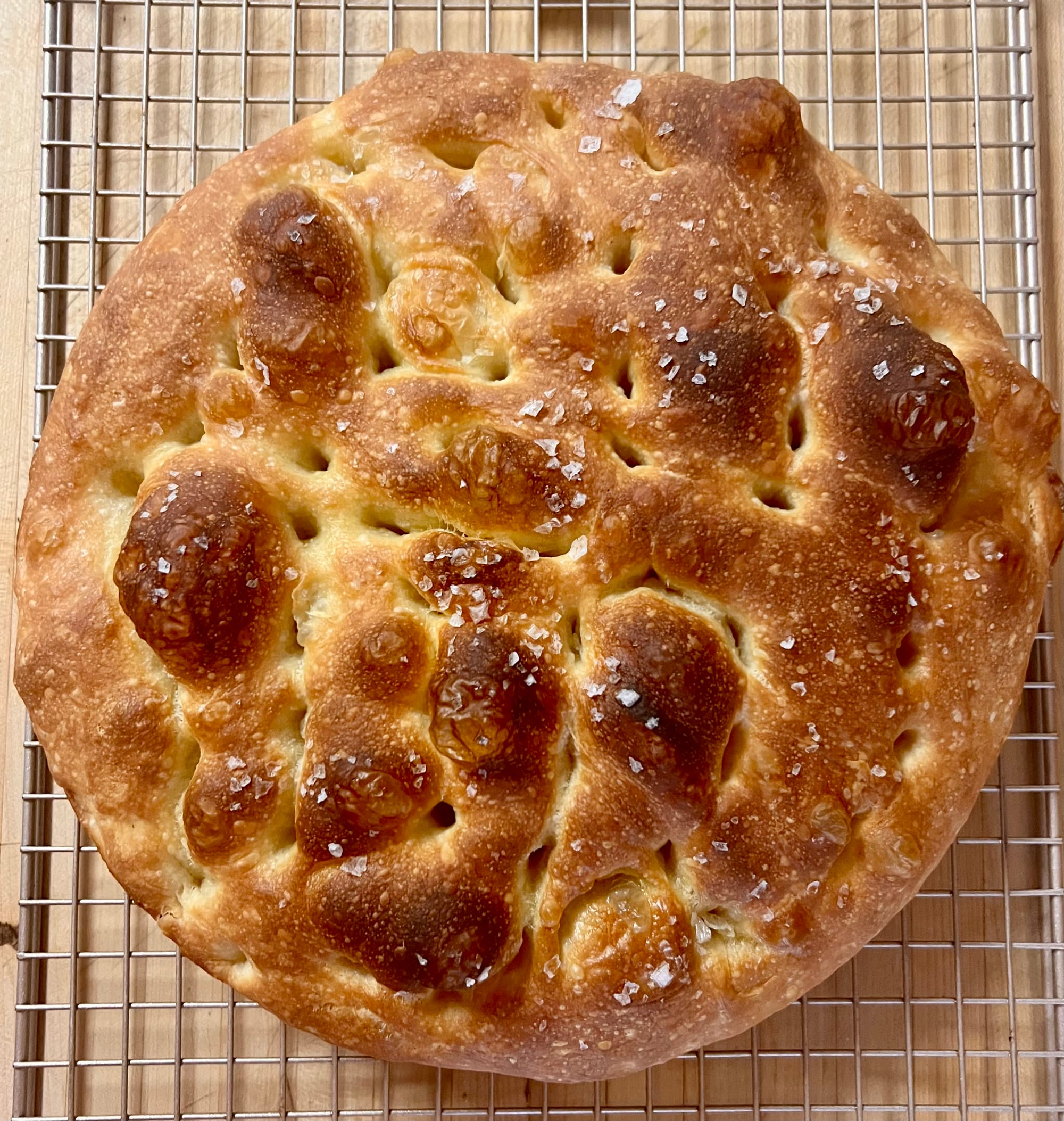 A round loaf of focaccia. There are big, deep brown bubbles on top, and lots of salt crystals.